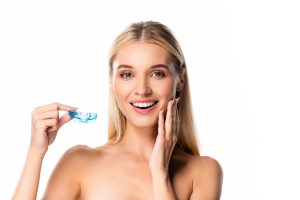 Mujer sonriente que sostiene en la mano un protector bucal de plástico azul transparente, sobre fondo blanco